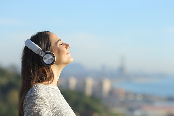 Woman listening to an audiobook while taking a deep breath outdoors.